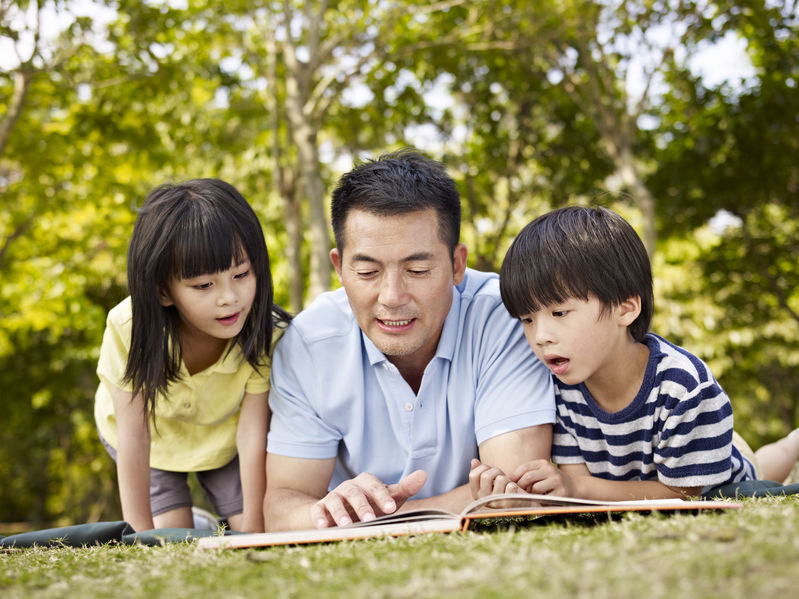 asian father and children reading book together