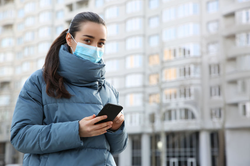 Woman with disposable mask and smartphone outdoors. Dangerous vi